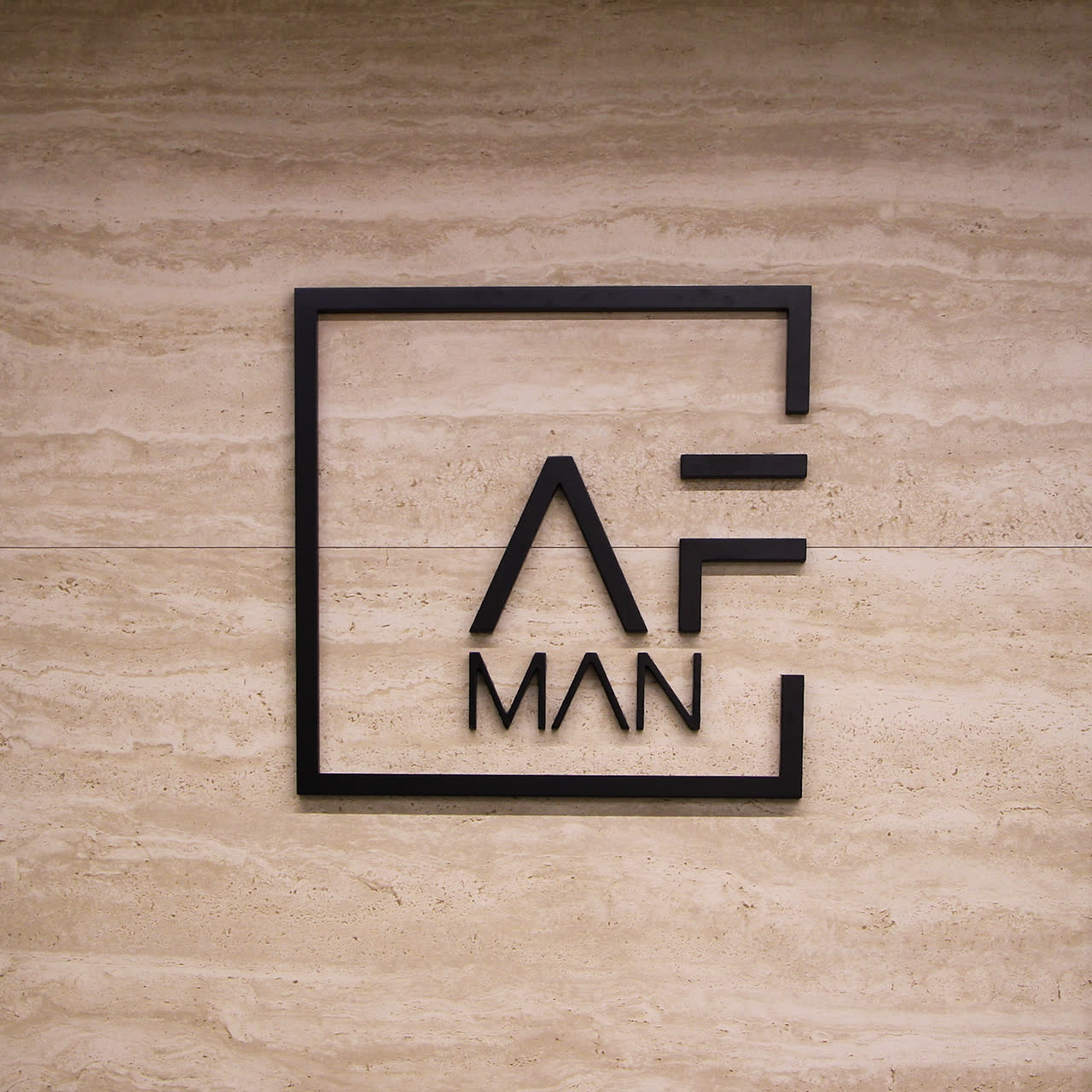 Logo AFMAN in metallo nero su parete in travertino